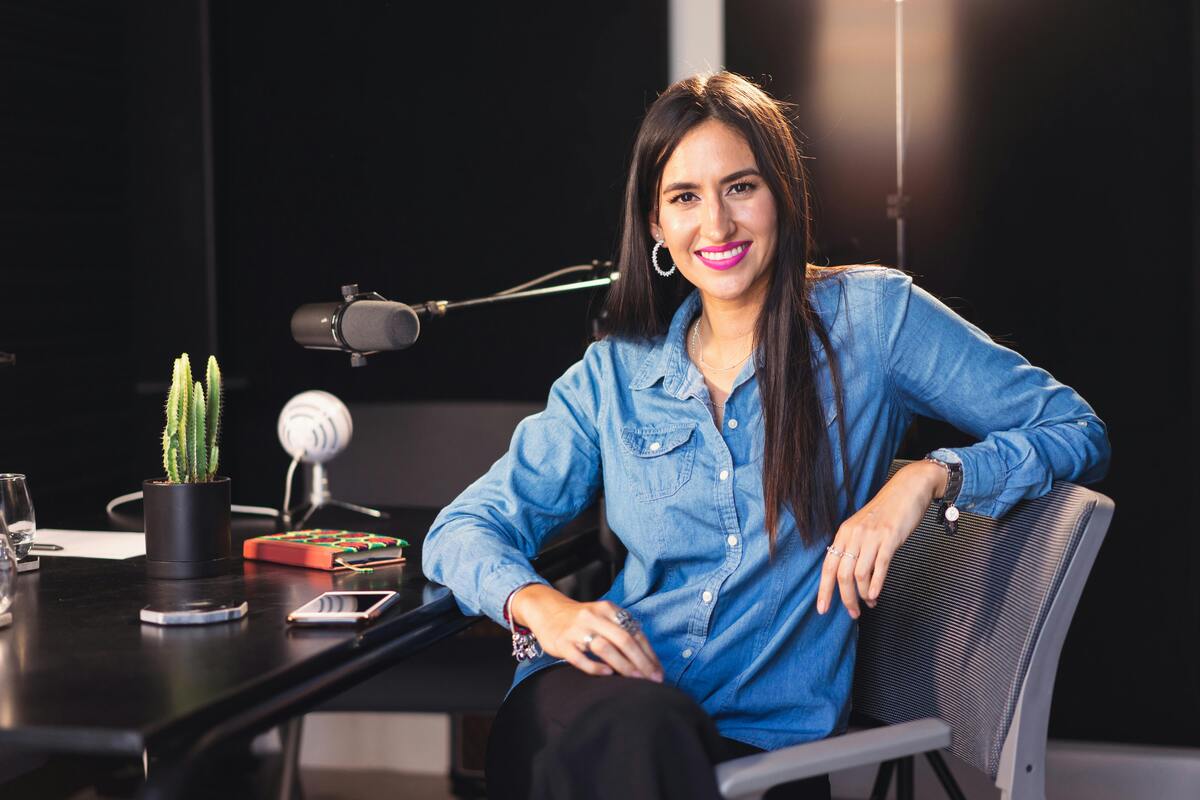 Smiling young woman in a recording studio with microphone and laptop, representing career paths in journalism and how to become a journalist.