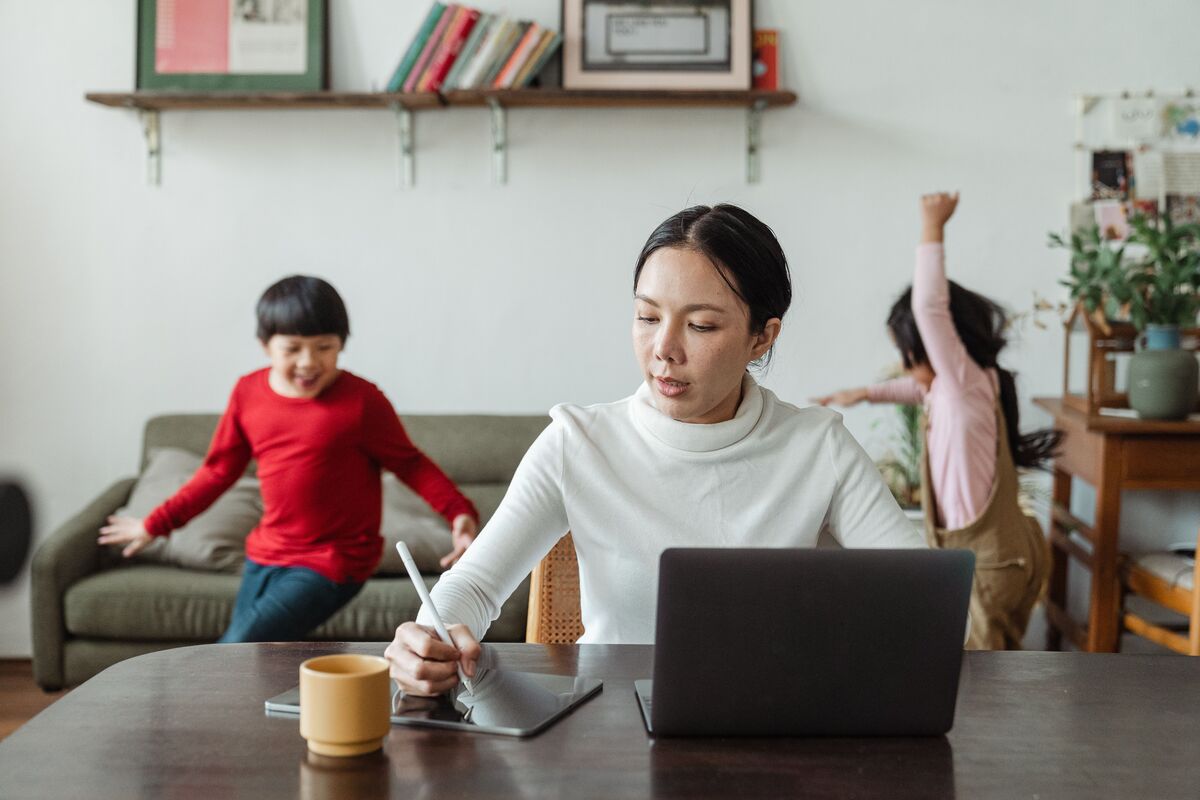 woman working from home with two children behind her, WFH meaning